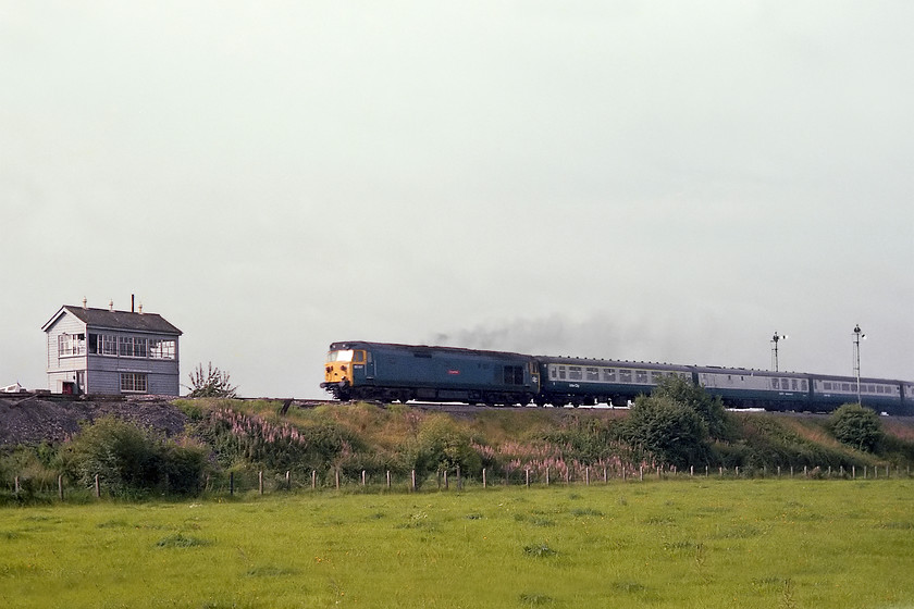 50017, 07.50 Paignton-London Paddington (1A07), Heywood Road Junction 
 Taken across the field from the elevated box at Heywood Road Junction just east of Westbury is 50107 'Royal Oak' working the 1A07 07.50 Paignton to Paddington. The arm lowered on the signal seen in the image indicates that the train has stopped at Westbury station rather than taking the cut-off route. Also note that the buffet/restaurant car is marshalled as the second coach of the formation. It was usual practice to find it here on an up Paignton working with it often being the first coach. 
 Keywords: 50017 07.50 Paignton-London Paddington 1A07 Heywood Road Junction