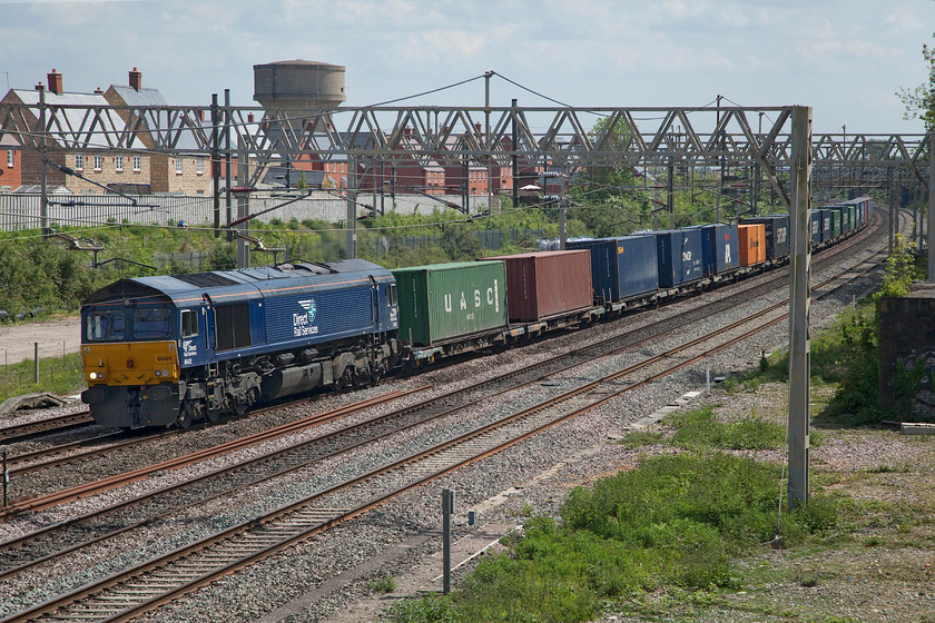 66425, 09.55 Tilbury-DIRFT (4M07, 4L), site of Roade station 
 66425 is my most photographed members of the class and I have many local images of it undertaking various duties. Here it is seen passing the site of Roade station leading the 4M07 09.55 Tilbury to Daventry Rail Freight Terminal. Despite the sun, there was a lot more high cloud about today and it was very warm for early May making it feel distinctly humid. Indeed, not long after this photograph was taken, there was a hefty shower spoiling people's appropriately socially distanced VE street party celebrations. 
 Keywords: 66425 09.55 Tilbury-DIRFT 4M07 site of Roade station DRS Direct Rail Services