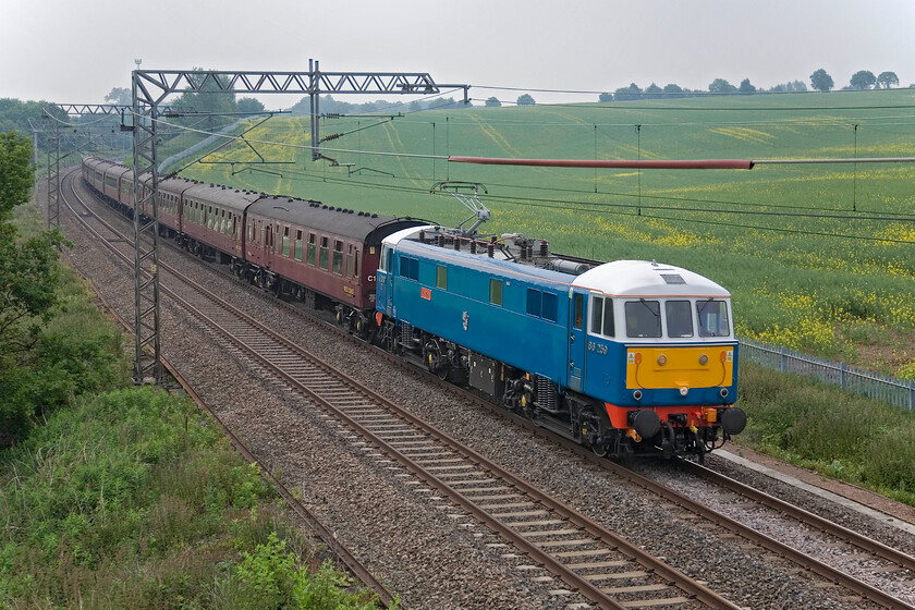 86259, outward leg of The Cumbrian Mountain Express 06.26 London Euston-Carlisle (1Z86), Milton Crossing 
 It may be just a day off the longest day but the weather on this June morning is not reciprocating! 86259 'Les Ross/Peter Pan' is seen passing Milton crossing just north of Roade with the outward Cumbrian Mountain Express. The weekday charter left Euston at 06.26 heading for Carlise with Black 5 46115 taking over at Carnforth. 
 Keywords: 86259 The Cumbrian Mountain Express 06.26 London Euston-Carlisle 1Z86 Milton Crossing AL6 Peter Pan Les Ross