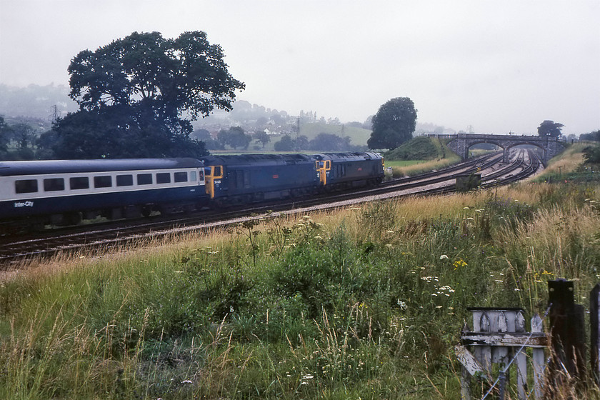 50001 & 50025, 16.45 Plymouth-London Paddington (1A57), Aller Junction 
 I did not usually take many 'going-away' photographs but double-headed 50s would have got me reaching for the wind-on lever on the Zenith camera! Taken from the small car park where the Aller Junction signalmen parked their cars, 50001 'Dreadnought' and 50025 'Invincible' accelerate away towards Newton Abbot leading the 16.45 Plymouth to Newton Abbot. As can be seen, the sea mist has drifted in creating a particularly miserable afternoon scene. This is a reverse view of a number of photographs that I took a couple of months previously, see..... https://www.ontheupfast.com/p/21936chg/29422479804/x50019-14-00-penzance-birmingham Unfortunately, the lovely twin arch stone occupation bridge that I spent a very pleasant few hours on back in May 1980 has now been knocked down with a stonking great big dual carriageway obliterating the land to the right. 
 Keywords: 50001 50025 16.45 Plymouth-London Paddington Aller Junction Dreadnought Invincible 1A57