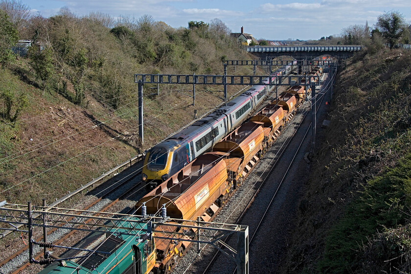 221110 and 221118, VT 14.18 London Euston-Birmingham New Street (1T43, 1E) & 66565, ballast train, Hyde Road bridge 
 Voyagers 221110 and 221118 work the 14.18 Euston to Birmingham New Street Avanti West Coast on the down slow line that will take it via Northampton rather than the more normal Weedon loop. The reason is clear to see with engineering works closing the fast lines at Roade. 66565 is seen reversing a short rake of loaded HQA(E) ballast wagons back to the work site just beyond the A508 bridge in the village of Roade. 
 Keywords: 221110 221118 14.18 London Euston-Birmingham New Street 1T43 66565, ballast train Hyde Road bridge AWV Avanti West Coast Voyager