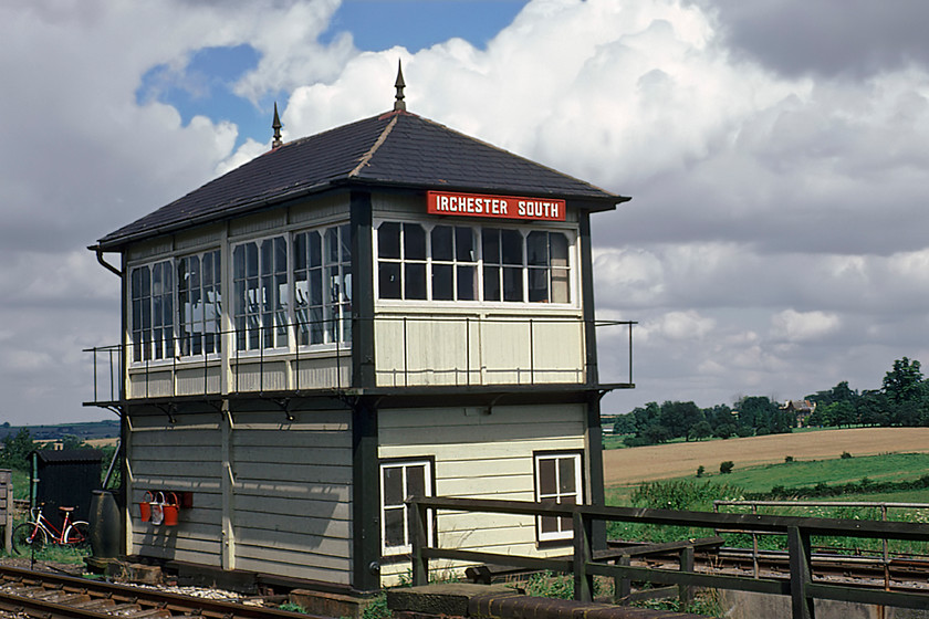 Irchester South signal box (Mid, 1881) (Courtesy of GGV) 
 Irchester South signal box was located at a very remote spot with no vehicular access so signalmen would have to either walk to work or ride their wife's red bike as is the case on the day of our visit! For those interested in its location, it was at the following Ordnance Survey grid reference SP938652. It was located in between the slow and fast lines where the former just begin to diverge as they take their slightly different route south utilising Sharbrook tunnel. In this photograph, the 1881 Midland box looks remarkably original with its external gallery and finials still in place. It was closed on 06.12.87 but due to its remote location remained in situ for sometime after this date relatively immune from the scourge of vandals who could not be bothered to wander across fields to get to it! The building in the background, partially surrounded by trees, is Knuston Hall owned by Northamptonshire County Council. Little did I know when I took this photograph that I would visit this historic house many times in my working career ten years on! 
 Keywords: Irchester South signal box Midland Railway