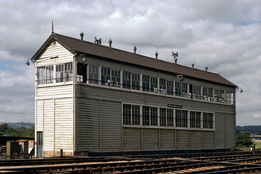 Newton Abbot East signal box (GW, 1926) 
 The very impressive Newton Abbot East signal box is seen with the town's racecourse just visible to the extreme right. The box opened in 1926 along with the West signal box. Both were constructed when the station was extensively rebuilt by the GWR as a further effort to speed up its trains to the west. The box had a huge two hundred and six lever frame. The box was so long that it had two coal-burning stoves to keep the interior warm on cold winter nights. The box closed over the weekend on 01-04.05 87 with the newly built Exeter Panel taking over control of the signalling. I am not at all sure how Graham and I got to this position to take this photograph? 
 Keywords: Newton Abbot East signal box