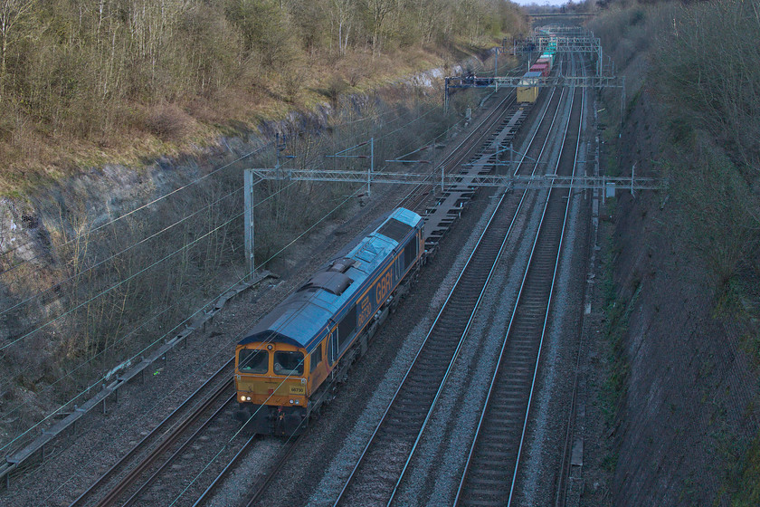 66730, 10.36 Felixstowe North-Hams Hall (4M23, 69L), Roade cutting 
 66730 'Whitemoor' leads the 10.36 Felixstowe to Hams Hall Freightliner through a very dark Roade cutting. Despite the lengthening days (British summertime begins on Sunday), the depths of the cutting is still very dark contrasting with the top of the cutting walls bathed in the warm afternoon sunshine. 
 Keywords: 66730 10.36 Felixstowe North-Hams Hall 4M23 Roade cutting Whitemoor GBRf