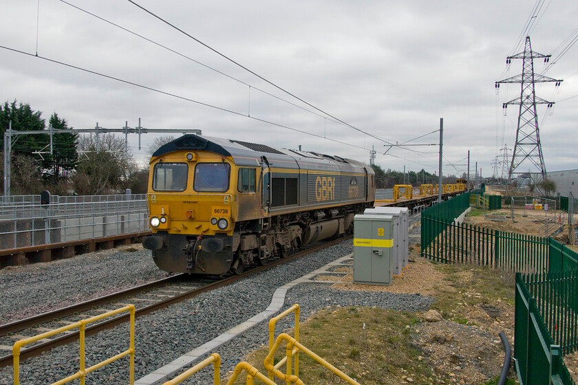 66738, 11.32 Whitemoor Yard-Doncaster Decoy (6E30, 23E), Werrington footbridge 
 Andy and I moved slightly further south of the classic location at Marholm from the bridge on Hurn Road to the new and somewhat over-engineered one in the middle of the Werrington industrial estate. Despite its gargantuan size, photographic opportunities are somewhat limited due to its huge parapets preventing views of the lines. One position that can be used is from the lower side of the bridge on the western side revealing a reasonable view of trains on the down Stamford line. 66738 'Huddersfield Town' is seen leading the 11.32 Whitemoor Yard to Doncaster Decoy that will run on this line as far as Helpston where it will cross to the down slow of the ECML. To the immediate left of the locomotive, the Werrington dive-under can be seen with the top of one of its colour lights juts in view. 
 Keywords: 66738 11.32 Whitemoor Yard-Doncaster Decoy 6E30 Werrington footbridge Freightliner Huddersfield Town