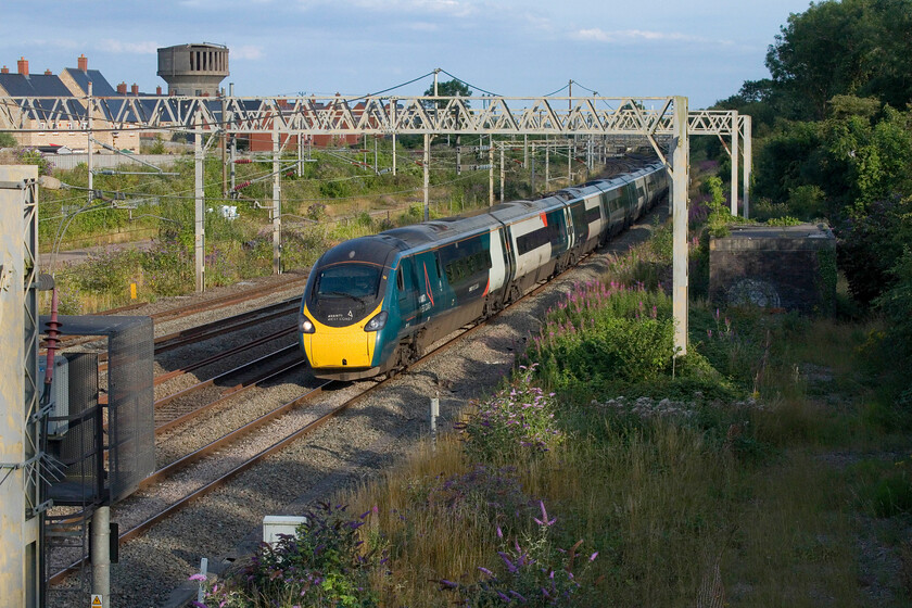 390134, 17.34 London Euston-Liverpool Lime Street (1F32, 21L), site of Roade station 
 In some really warm and welcome evening sunshine 390134 passes Roade working the 17.34 Euston to Liverpool Avanti service. Regular viewers of my site will recognise one of Roade's two water towers in the background. However, close examination reveals that work is taking place to turn it into a private residence with huge chunks of the concrete now removed presumably for the addition of enormous tall windows. In addition, a section of the roof has been removed where a panoramic glass section looks like it will be installed. 
 Keywords: 390134 17.34 London Euston-Liverpool Lime Street 1F32 site of Roade station AWC Avanti West Coast pendolino