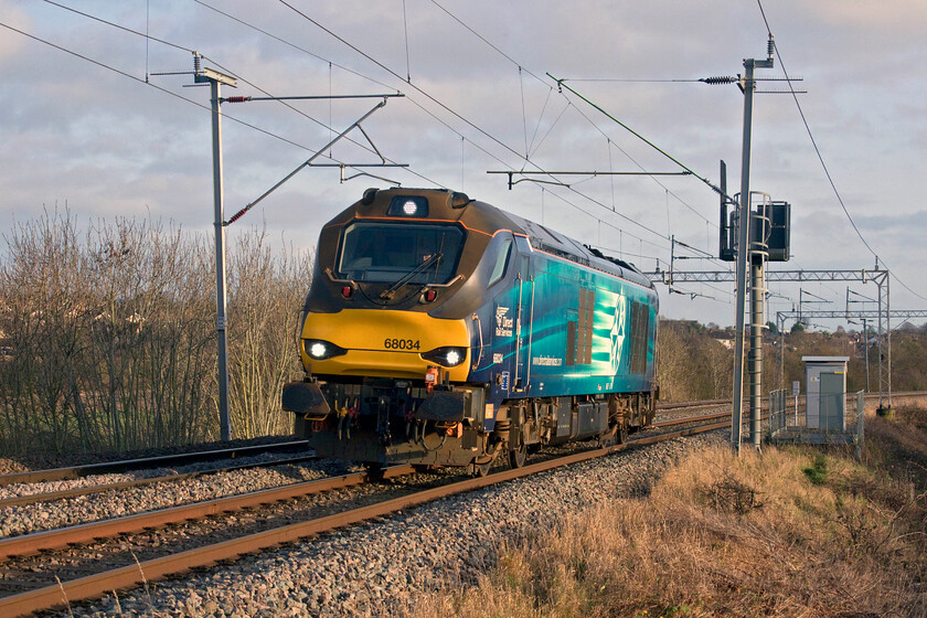 68034, 13.00 Wembley TMD-Crewe Gresty Bridge (0M34, 15E), Wilson's Crossing 
 I had been following the progress of this 0M34 (Thanks to Mike for the reporting number) on OTT as it had been moving pretty quickly northbound along the WCML slow lines. With a much-reduced timetable, I was wondering if it would put on the fast at Hanslope Junction but was pleased that it did not. 68034 running as the 13.00 Wembley to Crewe is seen racing away from Northampton on the rising gradient at Wilson's Crossing in some lovely winter sunshine. 
 Keywords: 68034 13.00 Wembley TMD-Crewe Gresty Bridge 0M34 Wilson's Crossing DRS Direct Rail services