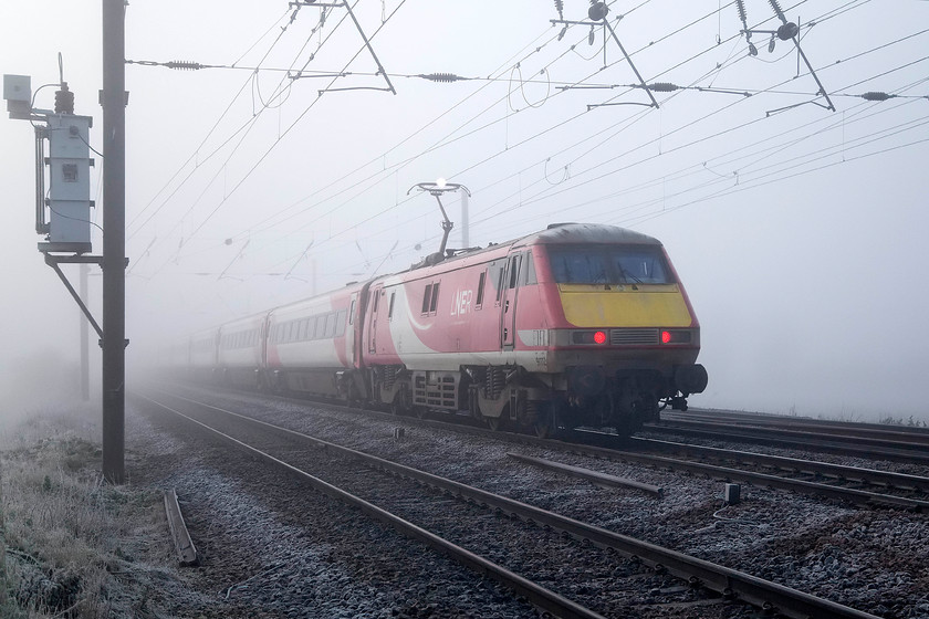 91112, VT 05.59 Newcastle-London KIng`s Cross (1Y08, RT), Holme Green Crossing TL192426 
 On a very foggy and very cold morning, 91112 propels the rear of the 05.59 Newcastle to King's Cross past Holme Green foot crossing that is just south of Biggleswade. Notice the pantograph's pannhead arcing as it collects power from the contact wire, an event that only occurs in sub-zero temperatures. 
 Keywords: 91112 05.59 Newcastle-London KIng`s Cross 1Y08 Holme Green Crossing TL192426 Virgin Trains East Coast