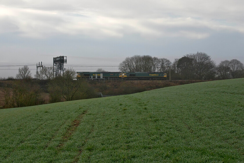 66534 & 66505, 10.45 Wembley Yard-Crewe Basford Hall (0Y62, 45E), Roade Hill 
 As I was walking across a field close to the line between Roade and Ashton I was aware of a train heading north. It emerged from the shallow cutting to the left in this view just in time for me to get the camera out. 66505 and 66534 'OOCL Express' run light engine as the 0Y62 10.45 Wembley yard to Crewe Basford Hall. It is clear in this photograph how grey and dull the day before Christmas was! Incidentally, I have just been reading about the construction of the extremely troublesome embankment seen in this photograph and of Roade cutting itself by the thousands of navvies who descended on this rural quarter of Northamptonshire from 1834. The history of the cutting is superbly documented in a new book written by Chris Hillyard and published by Roade History Society, see.... https://www.roadehistorysociety.org.uk/ 
 Keywords: 66534 66505 10.45 Wembley Yard-Crewe Basford Hall 0Y62 Roade Hill Freightliner OOCL Express