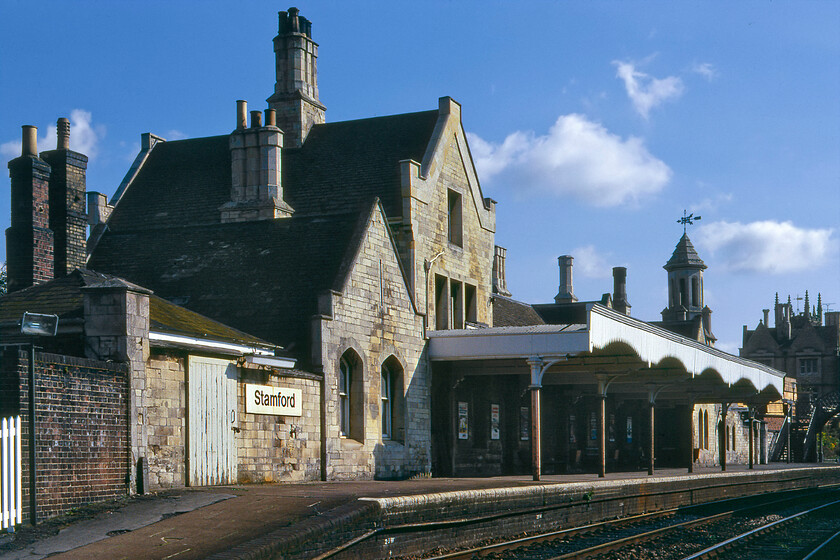 Stamford station from west 
 A view of Stamford station building taken from the western end. As it was a Sunday morning, it was very quiet with nobody about apart from the signalman in the box some distance behind where I am standing. Santon Woods mock Tudor design is now Grade 2 listed and looks very much as is seen here even down to its weathervane atop the conical turret that still bears the initials of the Syston & Peterborough Railway. In more recent years the station housed Robert Humms bookshop that specialised in rare and out-of-print railway books. I know that this bookshop is celebrated by railway enthusiasts and others alike but after visiting with my son I have to say what a rude and ignorant man the owner was asking my son not to touch the books. Has he no idea about how two nurture the love for books in the young? We promptly left the book open on a chair, and walked out of the shop with me not spending the cash that I had ready in my back pocket; what a way to run a business. Incidentally, in 2016 the bookshop vacated the station site so it no longer sullies a visit to the fine station. 
 Keywords: Stamford station from west