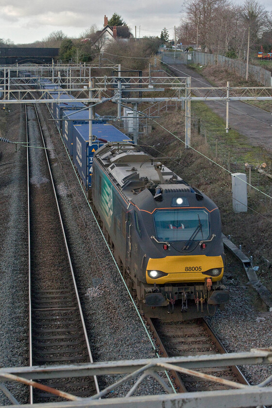 88005, 13.37 DIRFT-Tilbury (4L48, 25L), site of Roade station 
 The daily 4L48 13.37 (or thereabouts) Daventry to Tilbury docks Tesco Express has been operating for a number of years and is one of the most dependable freights to pass my home village of Roade just after lunchtime. However, what has begun to change is the motive power. Whilst it has been a DRS Class 66 for many years over the last eighteen months or so Class 88s have become regular performers on the train. 88005 'Minerva' leads the train out of Roade cutting into the late afternoon winter light on the up slow line almost catching me out due to its almost silent operation compared to a noisy and struggling 66! 
 Keywords: 88005 13.37 DIRFT-Tilbury 4L48 site of Roade station DRS Direct Rail Services Minerva