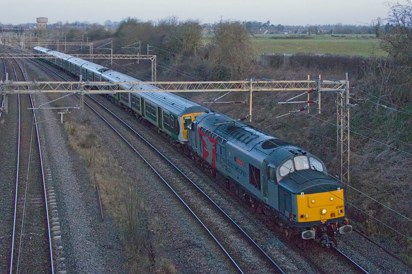 37884, 319457 & 319433, 07.58 Northampton EMD-Newport Docks (Sims Group) (5Q76, 59L), Victoria bridge 
 Nearly the end of the line for another pair of the venerable Class 319s. With the limited introduction to service of the Class 730s London Northwestern can dispose of the the 1980s BREL (York) constructed EMUs. Still wearing their London Midland liveries 319457 and 319433 are towed by 37884 'Cepheus' at a slow pace past Victoria bridge just south of Roade as the 07.58 Northampton EMD (Kingsheath) to Sims Group's yard in Newport Docks running as 5Q76. Apologies for the poor technical quality of this photograph but I had been attempting to capture one of these scrap trains for some time and the timings of this one were a bit marginal in terms of the time of day! 
 Keywords: 37884 319457 319433 07.58 Northampton EMD-Newport Docks Sims Group 5Q76 Victoria bridge Cepheus