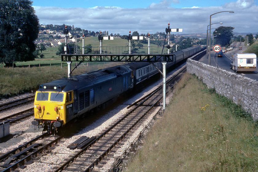 50045, 07.45 Kensington Olympia-St. Austell Motorail (1V34), Aller Junction 
 Behind the eight Mk. 1 coaches being hauled by 50045 'Achilles' are a number of Motorail flats that look healthily loaded with some of the finest cars of the era no doubt! The Class 50 (formally D445) is leading the 07.45 Kensington Olympia to St. Austell service past Aller Junction delivering another tranche of holidaymakers and their cars to the south-west for their summer break. The car and caravan combo making its way along the A380 towards Newton Abbot have not taken advantage of the train. According to contemporary records, the car towing the 1970's vintage caravan is a one-year-old Lancia of some kind.

There is an audio recording of this event on my youtube channel, see..https://youtu.be/c3yKbZyNRa4 
 Keywords: 50045 07.45 Kensington Olympia-St. Austell Motorail 1V34 Aller Junction Achilles Class 50 D445