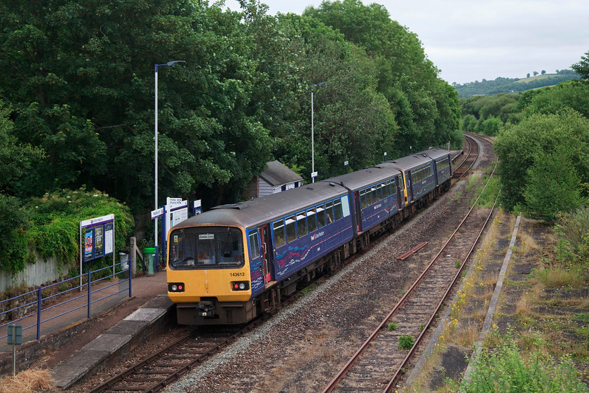 143612 & 143319, GW 07.00 Barnstaple-Exeter Central (2R89, RT), Yeoford 
 143612 and 143319 pauses at Yeoford station in deepest Devon with the 07.00 Barnstable to Exeter Central. For such a tiny village Yeoford once boasted a substantial three platform station complete with a large are of sidings. Standing on this bridge you could observe a procession of express trains heading westwards from London. This line was the 'other' L & SW route to the west avoiding the GW's line along the seawall of south Devon. Given the constant problems with the seawall there is serious consideration to this route being reinstated as a mainline. This would have avoided Cornwall and much of west Devon being completely cut off from the network for two months during early 2014. 
 Keywords: 143612 143319 2R89 Yeoford