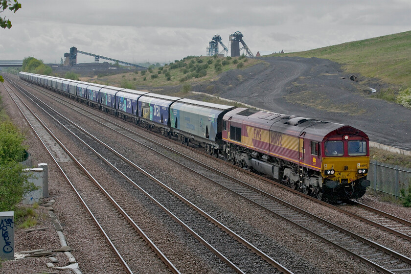 66092, 14.33 Drax PS-Immingham Biomass (4R53, 1L), Cuckoo bridge SE660116 
 66092 is seen under threatening skies passing Stainforth wearing its original 'as delivered' livery. It is amazing that despite being in operation for twenty-two years that it still in its EWS livery complete with the three beasts logo on the cab side given that the company was taken over by DB way back in June 2007! The Class 66 is hauling the 4R53 14.33 Drax power station to Immingham biomass empties. On arrival, the converted coal wagons will be loaded with more imported North American biomass pellets for delivery to the nearby power station to keep its furnaces burning. In this view, the former Hatfield Colliery is seen. Despite the mine now being closed and the shafts backfilled the two headstocks remain in place. They will continue to stand as a reminder to the local area's proud industrial heritage as they are both now Grade II listed, see.... https://historicengland.org.uk/listing/the-list/list-entry/1430590 The recently planted slope in the middle distance behind the train marks the spot where a huge slump of material took place in February 2013. Approximately 1,000,000 cubic metres of mudstone slipped and engulfed the quadruple tracks necessitating a huge clear-up and total reconstruction of the line that took some six months to complete. 
 Keywords: 66092 14.33 Drax PS-Immingham Biomass 4R53 Cuckoo bridge SE660116 EWS