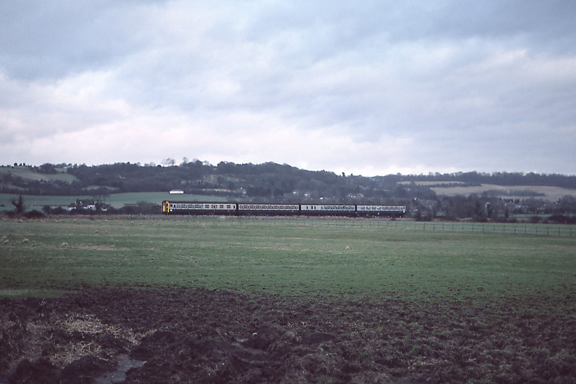 EMU, 13.55 London Victoria-Ashford, Charing TQ943492-01.01.81 
 Looking across the fields towards the village of Charing sees an unidentified Southern Region EMU approaching the station working the 13.55 Victoria to Ashford service. Unfortunately, I do not know what class of EMU is seen in this photograph. If anybody can advise me I will update my records. 
 Keywords: EMU 13.55 London Victoria-Ashford, Charing TQ943492