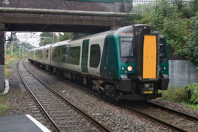 350234, LN 12.24 London Euston-Rugeley TV (9K60, RT), Landywood station 
 350234 has taken nearly three hours to make the journey from Euston to reach Landywood station. It is seen leaving the staggered northbound platform forming the 12.24 to Rugeley Trent Valley. If I was a resident of Rugeley and wanted to get to London I suspect that I would choose one of the hourly services that take the Trent Valley route on a train to and from Crewe rather than go on the infinitely slower and stopping route via New Street. However, as a local, I also think that I would welcome the much enhanced electric services to and from the West Midlands that have been available to me since the May timetable change. 
 Keywords: 350234 12.24 London Euston-Rugeley Trent Valley 9K60 Landywood station