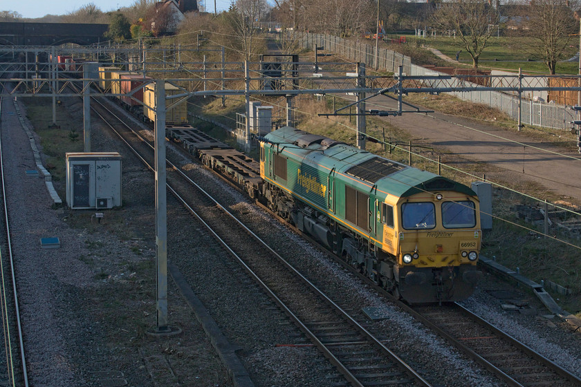 66952, 12.57 Birch Coppice-Felixstowe North (4L57, 1L), site of Roade station 
 66952 emerges from Roade cutting into the evening sunshine at the site of the former station leading the 4L57 12.57 Birch Coppice to Felixstowe North. Notice the recreation ground in the background of the image. On a warm spring Friday afternoon this would usually be packed with youngsters and families enjoying the facilities. In line with the COVID-19 limitations, this is firmly off limits and, judging by this view, the rules are being followed with nobody in sight. 
 Keywords: 66952 12.57 Birch Coppice-Felixstowe North 4L57 site of Roade station Freightliner