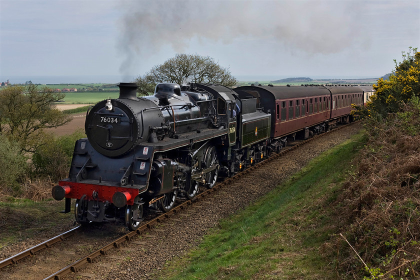 76034 (76084), 10.30 Sheringham-Holt, Kelling bank 
 Class 4MT 76084 (and not 76034 as is being worn by the locomotive) roars up Kelling bank with the 10.30 Sheringham to Holt train. It's a shame that the sun has just lost its edge going behind some high cloud. However, this disappointing lighting can be improved using Photoshop. However, it's not all bad news because in strong sunshine the problem of very high contrast becomes an issue that often manifests itself particularly badly with a gloss black locomotive. 
 Keywords: 76034 10.30 Sheringham-Holt Kelling bank British Railways Standard Class 4MT 76084