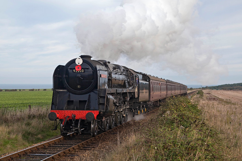 92203, 10.30 Sheringham-Holt, Weybourne TG122424 
 92203 'Black Prince' charges up the sharp gradient rising towards Weybourne station with the10.30 Sheringham to Holt. With the North Sea in the background this chilly autumn scene takes on a certain atmosphere. Notice the red poppy adorning the front of the 9F as the picture was only take two weeks prior to Remembrance Sunday. 
 Keywords: 92203 10.30 Sheringham-Holt Weybourne TG122424