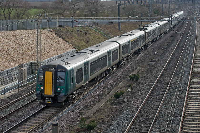 350257 & 350404, LN 09.49 London Euston-Northampton (1N42, RT), Ashton Road bridge 
 Utilising the flip-out screen on the camera and holding it up over the parapet of Ashton Road bridge has enabled me to photograph the 09.49 Euston to Northampton 1N42 service. The service is led by 350257 that will soon be going off-lease along with all the other 350/2 subset partially replaced by the smaller number of the 350/4 subset that was cascaded from TPE. One of these ten units, 350404, brings up the rear of the train. 
 Keywords: 350257 350404, LN 09.49 London Euston-Northampton 1N42 Ashton Road bridge