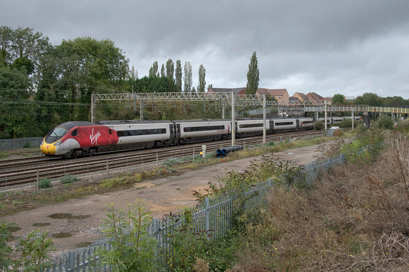 390042, VT 10.38 Liverpool Lime Street-London Euston (1A14, 8L), site of Roade station from former Pianoforte site 
 Yet another shower rolls in to dampen my day as 390042 passes Roade with the 10.38 Liverpool Lime Sreet to Euston. The photograph is taken from a bank created to facilitate the construction of a new housing estate. The site if the former Roade station is just beyond the footbridge in the background. 
 Keywords: 390042 10.38 Liverpool Lime Street-London Euston 1A14 site of Roade station from former Pianoforte site