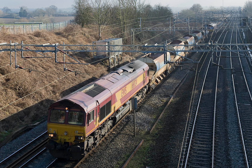 66024, 12.02 Willesden West London-Junction-Crewe Basford Hall, Victoria bridge 
 A short train composed of just five ballast wagons and a flat heads sedately north past Victoria bridge just south of Roade. 66024 leads 66078 working the 12.02 Willesden West London Junction to Crewe Basford Hall engineering train. This picture illustrates why I like taking pictures at this time of year. If this had been taken in July, yes the light would have been strong but the whole of the underframe and the front of the locomotive and wagons would have been virtually totally black with a loss of all detail. Whereas, it is all lit with the detail clearly illuminated by the low sun angle. 
 Keywords: 66024 12.02 Willesden West London-Junction-Crewe Basford Hall Victoria bridge