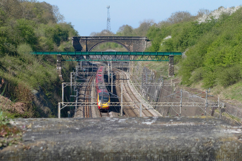 Class 390, VT 10.40 Glasgow Central-London Euston (1M11), Roade cutting 
 An unidentified class 390 Pendolino passes through a very spring-like Roade cutting working the 10.40 Glasgow Central to Euston. By using a zoom lens the various structures in the cutting have been briught together foreshortening it considerably. Unfortunately, this has reduced the depth of field so the vast stone parpapet of the bridge I am standing on is out of focus. 
 Keywords: Class 390 10.40 Glasgow Central-London Euston 1M11 Roade cutting Virgin Trains Pendolino