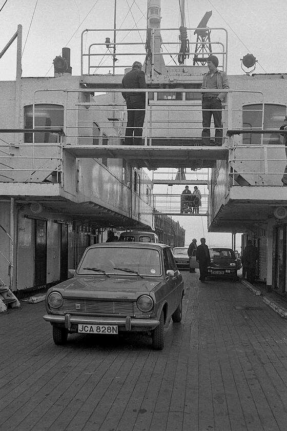 Car deck, MV Farringford 
 The driver of the blue 1975 Simca peers back over his left shoulder as he reverses the car along the deck of MV Farringford whilst it is loaded at New Holland Pier prior to the 16.50 sailing to Hull Corporation Pier. This view looking along the length of Farringford's car deck reveals its unusual design. It was never seen as an attractive design but was functional both when as a front and rear loading vessel whilst in use on the Lymington-Yarmouth Isle of Wight route and here on the Humber after conversion to a more awkward side-loading configuration. 
 Keywords: Car deck MV Farringford Sealink