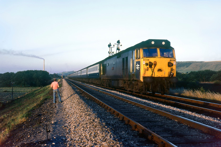 50041, 18.35 London Paddington-Newton Abbot (1B40), Hawkeridge East Junction 
 50041 'Bulwark' leads the 18.35 Paddington to Newton Abbot 1B40 service into Westbury having left the mainline at Heywood Road Junction in the distance. The train is just passing the bracket that has the Heywood Road home and the Westbury North distant pulled off for access to the station with the submissive lower doll with the arms controlling access to the sharp Hawkeridge curve leading to the Westbury-Bathampton (Avon Valley) route. Graham is seen in front of me having just taken his photograph with both of us flagrantly trespassing on this fine summer evening! In the background is the tall chimney of Westbury cement works with the smoke drifting indicating that a warm south-easterly wind was blowing. A picture taken some ten months later looking in the other direction from a passing train can be seen at.... https://www.ontheupfast.com/p/21936chg/30022860857/x38-t-50044-17-52-london-paddington 
 Keywords: 50041 18.35 London Paddington-Newton Abbot 1B40 Hawkeridge East Junction Bulwark Westbury cement works