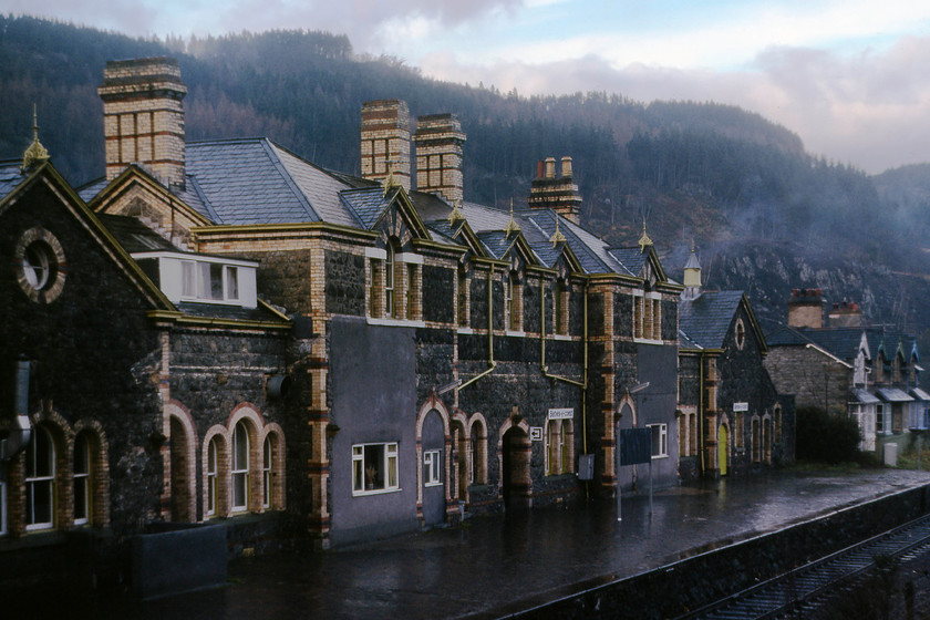 Betws-y-Coed station 
 With the mist and low cloud mixing with the smoke from chimneys Betws-y-Coed station nestles in the bottom of the Conwy Valley. It was opened in 1868 LNWR but by the time I took this photograph the building had been rationalised and was somewhat run-down. I am standing on the footbridge that joined the up and down platforms that, by this stage, merely provided access to the adjacent Conwy Valley Railway Museum as the line had been singled. Now the station has been much improved with a large canopy reinstalled. The building functions as a caf, visitors centre, bed and breakfast accommodation and is the home for a number of small retail outlets. Passenger numbers have been on the rise but will take a dive during 2019 caused by the four month closure of the Conwy Valley line due to extensive damage caused by flooding as a result of Storm Gareth in March. 
 Keywords: Betws-y-Coed station