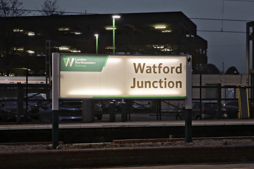 Illuminated running in sign, Watford Junction station 
 A large illuminated running-in sign is seen at the north end of Watford Junction station. I am not quite sure why I was attracted to take this photograph but I think that it was the contrast between the bright illumination of the sign and the dark background. I am also surprised that the internal illumination of the sign appears to be 'old school' fluorescent tubes. I would have thought that they might have been replaced by some sort of LED units by now. 
 Keywords: Illuminated running in sign Watford Junction station