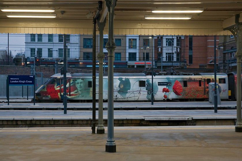 91111, GR 09.00 London King's Cross-Newcastle (1S09), London King's Cross station 
 Having just seen one celebrity Class 91 at King's Cross photographed in the previous image another one is observed. Again sporting some superb vinyl graphics 91111 'For the Fallen' will lead the 09.00 to Newcastle. Being eight o'clock in the morning and only a couple of weeks or so before the shortest day it is only just about half-light. 
 Keywords: 91111 09.00 London King's Cross-Newcastle 1S09 London King's Cross station VTEC For the Fallen Virgin Trains East Coast