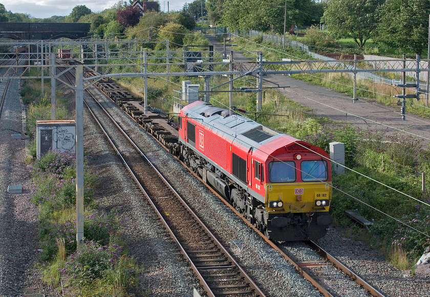 66182, 13.20 Trafford Park-London Gateway (4L56, 6E), site of Roade station 
 DB liveried 66182 brings the 13,20 Trafford Park to Felixstowe 4L56 through Roade exiting the fabled cutting and passing the site of the village's former station. I never like images of 'liner service that are unloaded at the front making it like it's a light engine move and unbalancing the scene! 
 Keywords: 66182 13.20 Trafford Park-London Gateway 4L56 site of Roade station