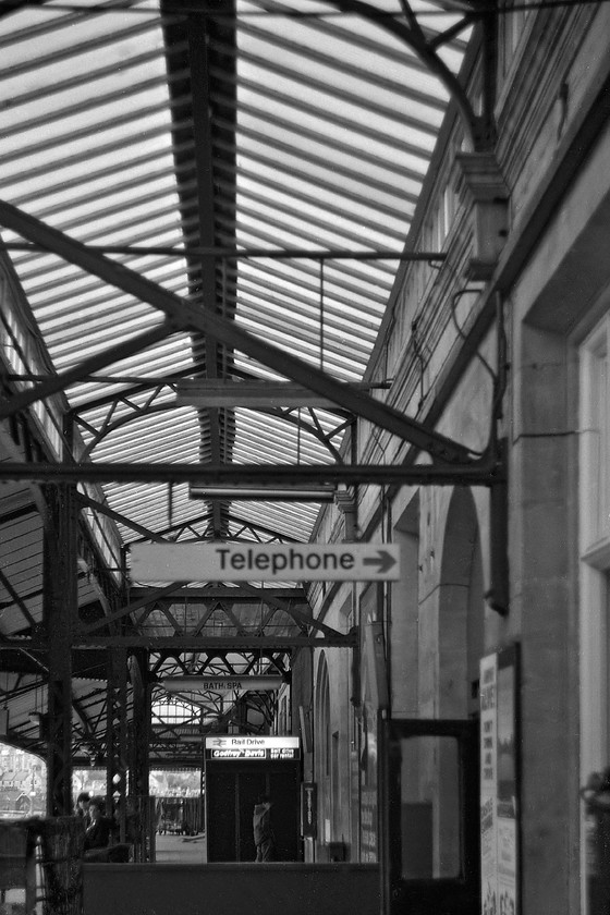 Under-canopy, down platform, Bath Spa station 
 The under-canopy of Bath Spa's down platform reveals a quiet scene. The roof seen here is a later addition with the original Brunel designed overall timber roof having been removed as early as 1897. Notice in this scene, the Godfrey Davis car hire sign. This was a familiar name from this era but one that was absorbed by Europcar in 1981. 
 Keywords: Under-canopy down platform, Bath Spa station