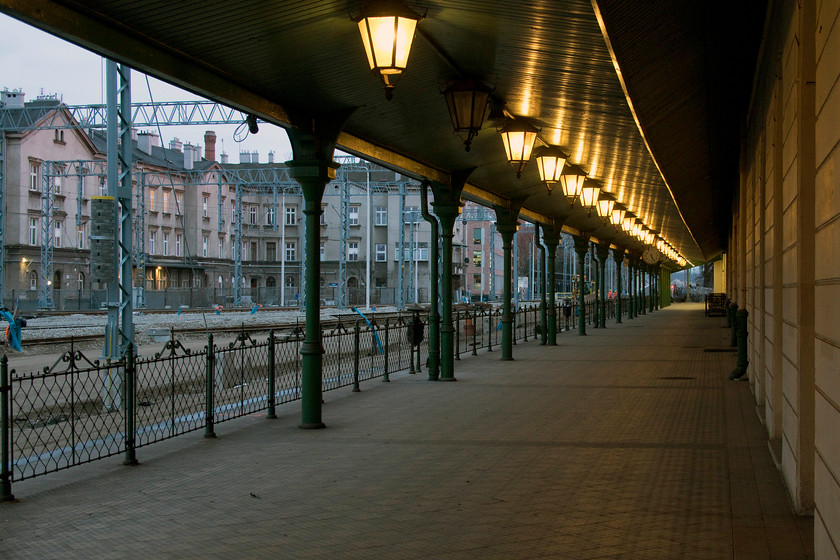 Former platform old Krakw Glwny station 
 The former main platform at Krakw Glwny station is seen lit but devoid of passengers and any signage as it was finally closed in 2014. The new station that is more of transport interchange also has direct access into the huge Galeria Krakowska shopping centre all of which is directly behind where I'm standing. Notice that there are very few tracks laid on the ballast behind the railings. The throat of the station to the south was in the process of complete renewal with only two running lines in use. This led to some inevitable cancellations with a number of bustitutions from the station forecourt. Sounds very familiar doesn't it! 
 Keywords: Former platform old Krakw Glwny station