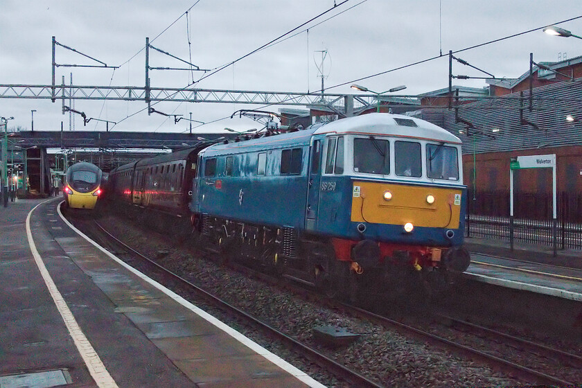 86259, outward leg of The Winter Cumbrian Mountain Express, 07.08 London Euston-Carlisle (1Z86, 5E) & 390151, VT 06.45 Wolverhampton-London Euston (1B04, 6L), Wolverton station 
 With the camera's ISO set to an eye-watering 25,600, I have really asked a little too much of it! It was half-light on a particularly dull January morning so this photograph is not of the finest quality. However, as I made the effort to get out to see 2022's inaugural Winter Cumbrian Mountain Express then it has made the cut! 86259 'Les Ross/Peter Pan' is seen heading the 1Z86 charter on the down slow through Wolverton station whilst 390151 'Unknown Soldier' has just got out of the way working the 1B04 06.45 Wolverhampton to Euston service that is on the up slow line. Remind me to stay at home on such a miserable morning and do something far more sensible than this next time, please! 
 Keywords: 86259 The Winter Cumbrian Mountain Express 07.08 London Euston-Carlisle 1Z86 390151 06.45 Wolverhampton-London Euston 1B04 Wolverton station Les Ross Peter Pan Unknown Soldier