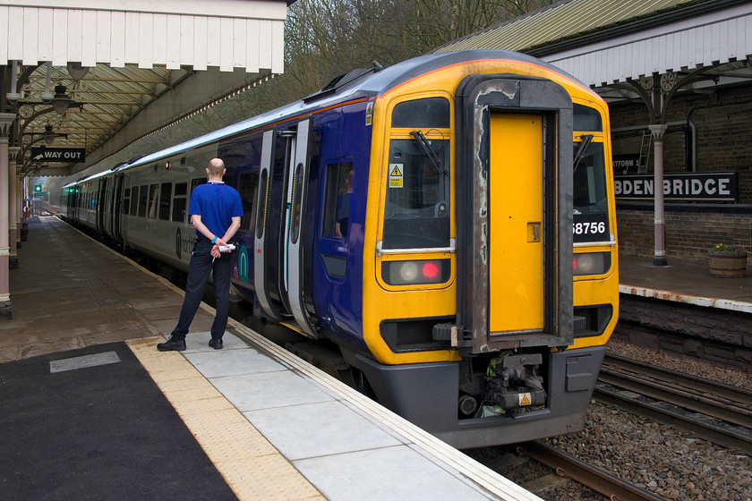 158756, NT 15.20 Manchester Victoria-Leeds (1U08, RT), Hebdon Bridge station 
 The conductor (guard to you and I!) looks on as his train, formed of 158756, waits to leave Hebdon Bridge station forming the 15. 20 Manchester Victoria to Leeds. Notice the wooden signage that adorns the station in evidence. I have not been carless in cutting off the running in board to the right. It was a deliberate decision as there was scaffolding behind the train that would have spoilt the picture. This scaffolding was being used by contractors who were undertaking a lot of work on the station, much of it to do with the installation of a lift. 
 Keywords: 158756 15.20 Manchester Victoria-Leeds 1U08 Hebdon Bridge station