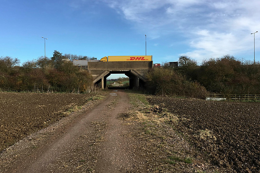 SMJ trackbed, M1 underbridge SP781524 
 With traffic crossing the bridge on the M1 motorway, the bridge that used to contain the SMJ railway is seen. I am standing on the former trackbed looking north east. The track has recently been reinforced and sees regular use as it provides access to the M1 wind farm that is behind me. 
 Keywords: SMJ trackbed M1 underbridge SP781524