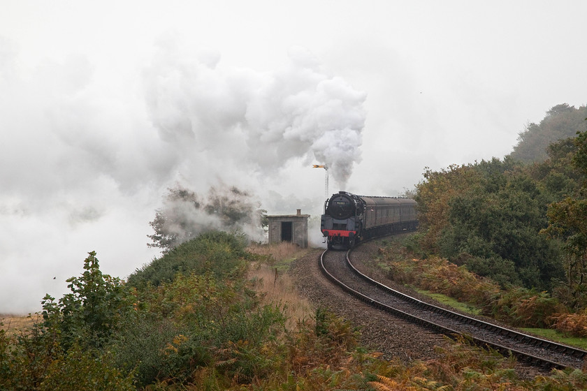 92203, 10.30 Sheringham-Holt, Kelling bank 
 In thick fog following a chilly and clear night, 92203 'Black Prince' storms up Kelling bank laying a thick layer of exhaust low in the sky that is forced down by the dense moisture laden air. It is leading the 10.30 Sheringham to Holt, the first steam hauled train of the day on the North Norfolk Railway. 
 Keywords: 92203 10.30 Sheringham-Holt Kelling bank