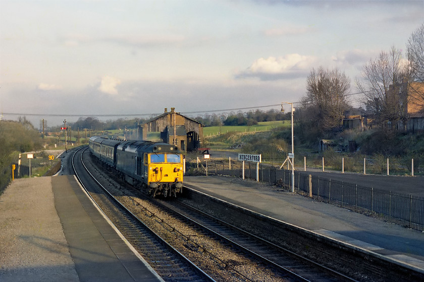 Class 50, unidentified down working, Hungerford station 
 In beautiful evening light, and unidentified class 50 races westwards through Hungerford station with a down working. Notice the extensive former yard and goods shed in the background. The station has undergone a huge programme of improvements in recent years and a large part of this former yard is now an inevitable car park for the commuters who head off to Reading and London every morning. 
 Keywords: Class 50 unidentified down working Hungerford station