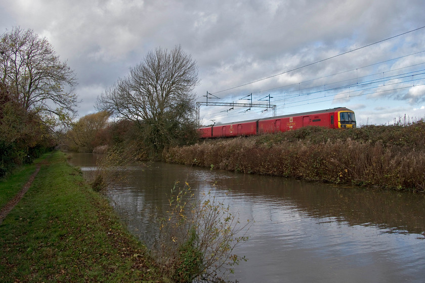 325008, 11.20 Crewe TMD-Willesden PDRC (5A91, 1E), Stretton Wharf SP432810 
 With the sun having dived behind a cloud, 325008 'Peter Howarth CBE' forms the 11.20 Crewe to Willesden 5A91 empty Royal Mail working. The train is seen passing a very autumnal scene near to Stretton Wharf on the Oxford Canal. Photographic opportunities on the classic short section of line are now limited with a ladder a requisite just to lift the subject clear of the rampant growth on the embankment. 
 Keywords: 325008 11.20 Crewe TMD-Willesden PDRC 5A91 Stretton Wharf SP432810 Royal Mail Peter Howarth CBE