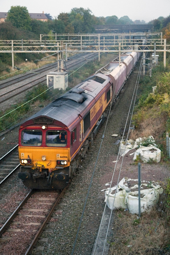 66007, 02.19 Peak Forest-Bletchley (6B10), site of Roade station 
 66007 leads the 02.19 Peak Forest to Bletchley aggregates train past the site of Roade station on a misty October morning just as the sun was beginning to come through. Notice the grab-bags of material next to the access gates on the right, yet another example of the expense wasted by the mis-managment of infrastructure planners. These particular bags had been here for months with weeds growing in them. Not only are they terrifically wasteful but also visually blight the railways. 
 Keywords: 66007 02.19 Peak Forest-Bletchley 6B10 site of Roade station