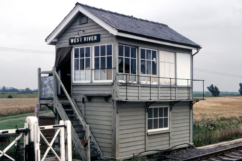 West River signal box (GE, date not known) 
 West River signal box was located just south of Ely on the Cambridge route. ISeen in its twilight years of operation, it was located at the eastern end of the small village of Little Thetford. It controlled access to a dead-end minor road that ended on the banks of the Ouse that flowed just beyond the wheat field in the background. The box is a standard Great Eastern design but I can find no date of construction unless anybody can advise me. Notice the blanket attached above the door and I cannot work out what item is seen hanging by a strap to the bottom of the steps. 
 Keywords: West River signal box Great eastern railway