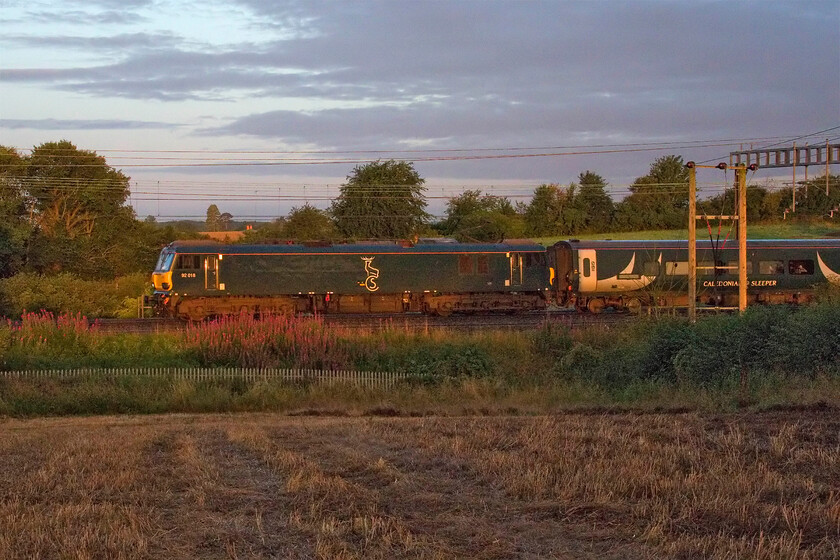 92018, CS 23.40 Glasgow Central & 23.42 Edinburgh Waverley-London Euston (1M11, 19E), between Roade & Ashton 
 with the sun having just raised itself above the horizon behind me a train that I have very few photographs of passes the countryside between Roade and Ashton in south Northamptonshire. The 1M11 or 'lowland' sleeper leaves Glasgow and Edinburgh as two separate services within a few minutes of each other coming together to form one long train to Euston at Carstairs Junction. On this particular morning, it is led by CS' 92018 that, like the stock, is doing its best to camouflage itself against the background! 
 Keywords: 92018 23.40 Glasgow Central 23.42 Edinburgh Waverley-London Euston 1M11 between Roade & Ashton Caledonian sleeper