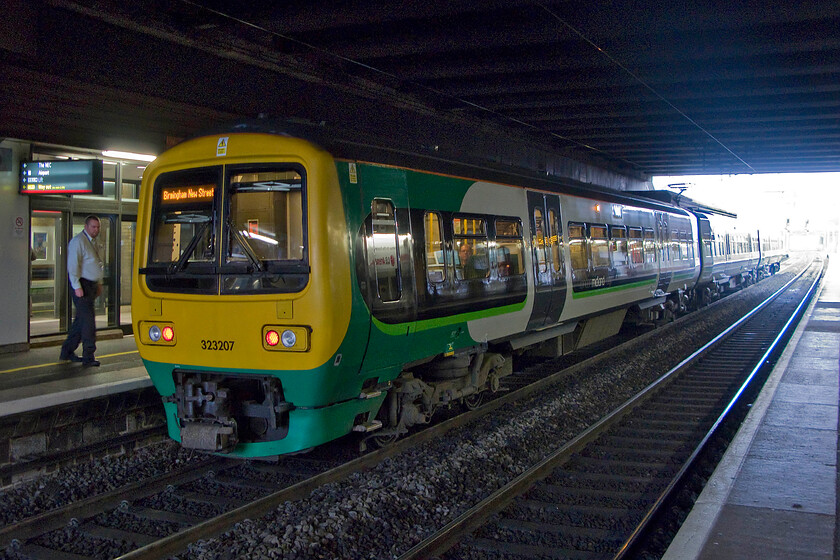 323207, LM 10.18 Birmingham Iinternational-Birmingham New Street (2I18), Birmingham International station 
 Inside the gloomy but functional interior of Birmingham International station, 323207 is seen waiting to depart as the 10.18 all-stations stopper to Birmingham New Street. I think that the guard may be a little underdressed as it was a chilly November day! 
 Keywords: 323207 10.18 Birmingham Iinternational-Birmingham New Street 2I18 Birmingham International station