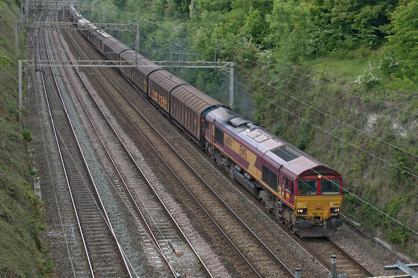 66094, 14.47 DIRFT-Dollands Moor (6M45, 103E), Hyde Road bridge 
 Making its usual racket as it passes through Roade cutting is the 14.47 Daventry to Dollands Moor 6M45 seen from the village's Hyde Road bridge with 66094 leading. This train runs empty with the Cargo Waggons (Sic) resonating and creating a very characteristic sound that usually draws the attention of the 'normals' should they happen to be crossing a bridge when it passes! 
 Keywords: 66094 14.47 DIRFT-Dollands Moor 6M45 Hyde Road bridge bottled water