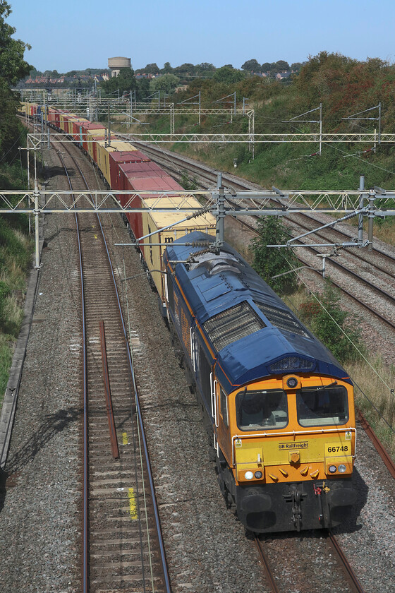 66748, 09.54 Hams Hall-Felixstowe North (4M13, 23L), Victoria bridge 
 In glorious hot sunshine 66748 'West Burton 50' leads the 09.54 Hams Hall to Felixstowe GBRf service on the up fast line past Victoria bridge just south of Roade. After a week of diversions with all traffic running on the 'old' route via Weedon control and signallers will no doubt be looking forward to the reopening of the Northampton loop and things able to return to normal! 
 Keywords: 66748 09.54 Hams Hall-Felixstowe North 4M13 Victoria bridge west Burton 50