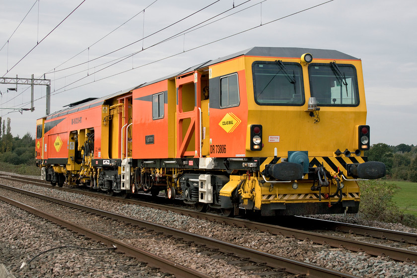 DR 73806, 13.34 Rugby DED-Watford Concrete (77L), Wilson's Crossing 
 Plasser & Theurer plain line tamper DR 73806 'Karine' passes Wilson's Crossing to the north of Northampton as the 13.34 Rugby to Watford Concrete move. This is a regular positioning move for a Tamper. I like the bright orange and contrasting yellow of the Colas machines; they certainly brighten up a dull September afternoon! 
 Keywords: DR 73806 13.34 Rugby DED-Watford Concrete Wilson's Crossing Karine