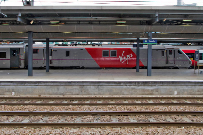 91125, GR 12.15 Leeds-London King`s Cross (1A29), Leeds station 
 A semi-pan photograph of 91125 propelling the 12.15 to King's Cross Virgin East Coast service out of Leeds station. Virgin has been operating the east coast services for nearly four months now but has only made limited progress re-painting the trains with just these rather dramatic vinyl flashes applied to the sides. 
 Keywords: 91125 12.15 Leeds-London King`s Cross 1A29 Leeds station Virgin East Coast